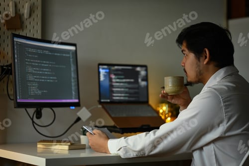 Preview: Bearded male software developer drinking coffee and coding at home office