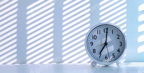 Preview: Sunlight and shadow on surface of white round table clock on white desk at morning time