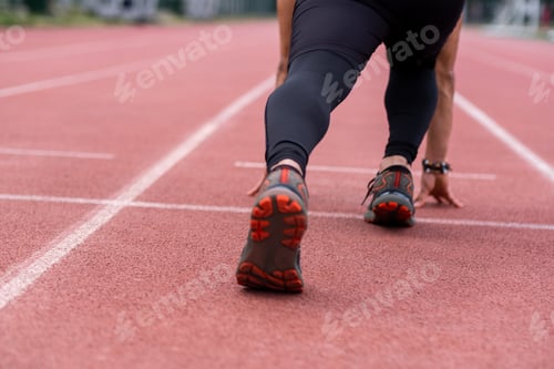 Preview: close-up professional sports man in low start position, poised to run track urban outdoor stadium.