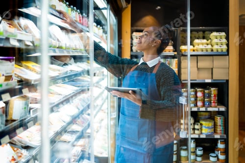 Preview: Saleswoman checking food products using digital tablet in organic supermarket
