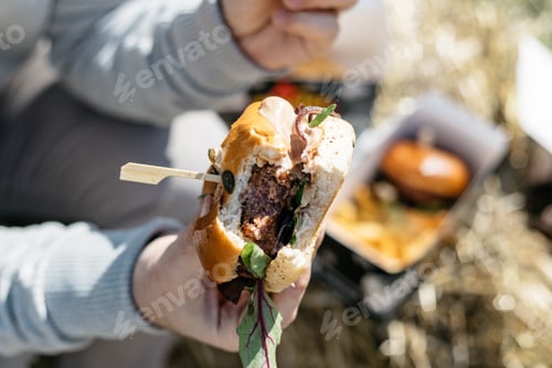Preview: Man eating out at a street food festival, burger amd fries.