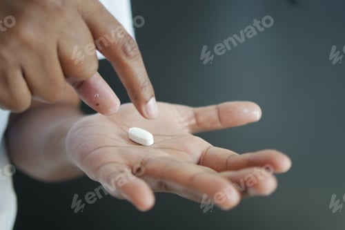 Preview: Close up of man hand holding capsule against black background