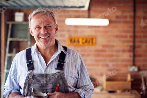 Preview: Portrait Of Mature Male Wearing Overalls In Garage Workshop With Hot Drink
