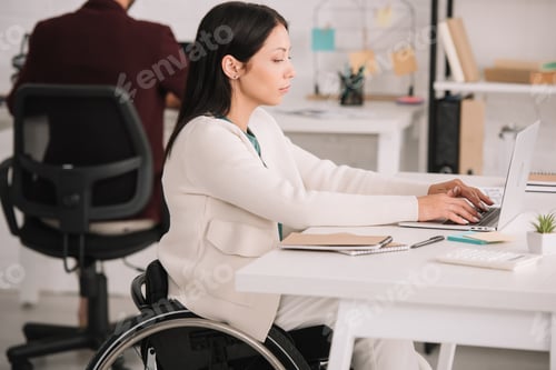 Preview: disabled businesswoman typing on laptop while sitting at workplace in offce