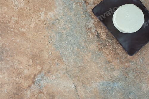 Preview: A white round cheese on dark plate on marble background