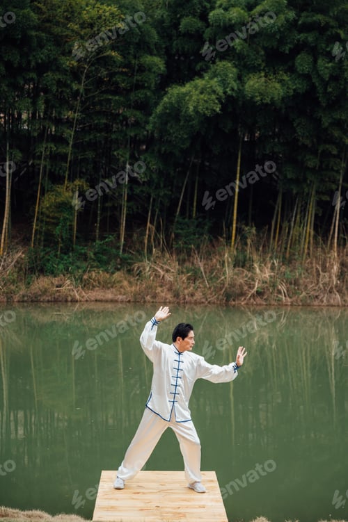 Preview: Asian senior man practicing tai chi outside by the river