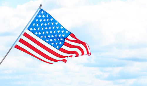 Preview: American flag near river on cloudy day. Space for text