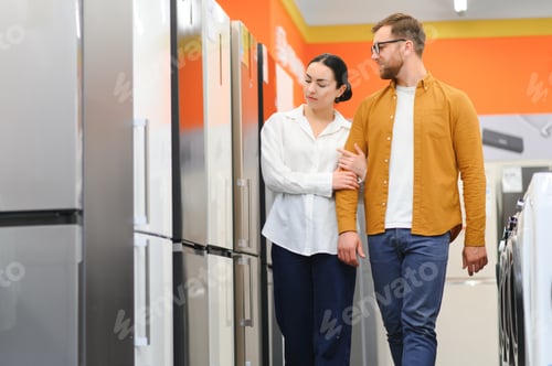 Preview: Young couple, satisfied customers choosing fridge in appliances store