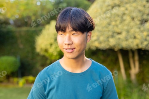 Preview: Smiling asian teenage boy in blue shirt enjoying time outdoors in garden
