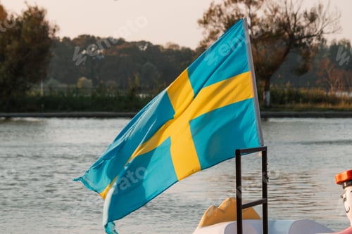 Preview: National flag of Sweden waving in wind at the shore in the soft sunshine