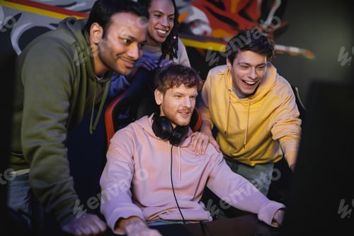 Preview: Multiethnic friends standing near friend playing computer game in cyber club