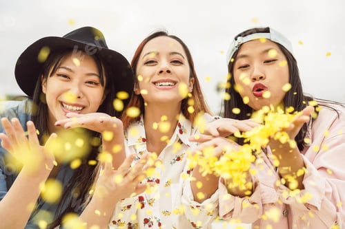 Preview: Happy Asian friends having fun throwing confetti outdoor
