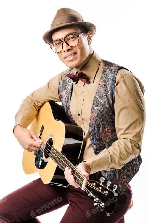 Preview: stylish mixed race male musician in hat and eyeglasses playing on acoustic guitar isolated on white
