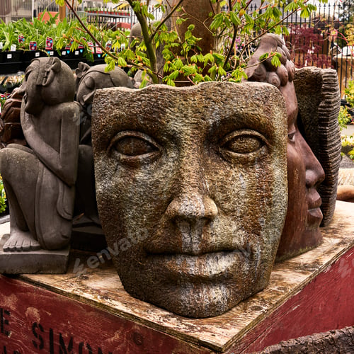 Preview: Garden decor, large cement sculpture of a face and creatures in the background for sale at a market.