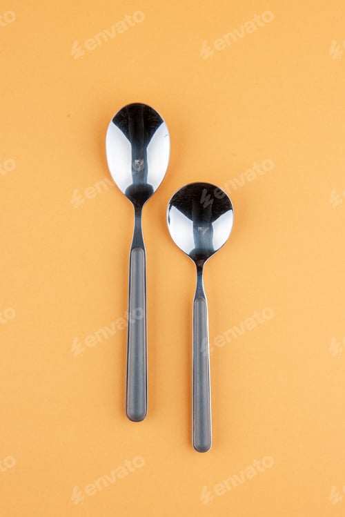 Preview: Overheadd view of stainless teaspoons lying side by side on golden background with free space