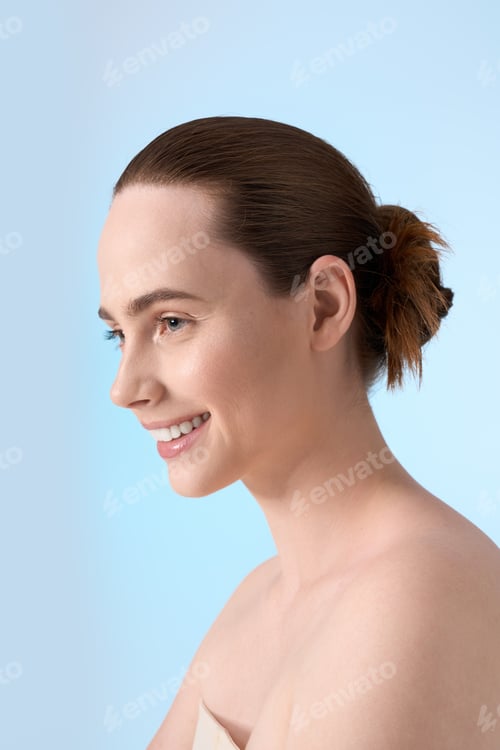 Preview: Young woman with fashionable hairstyle smiles brightly against a soft blue backdrop