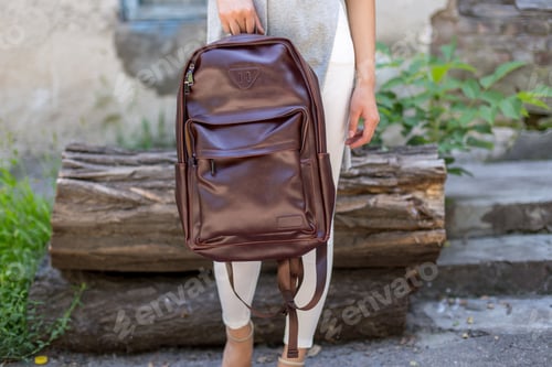 Preview: Woman holding brown leather backpacks in the hand. Unisex bag