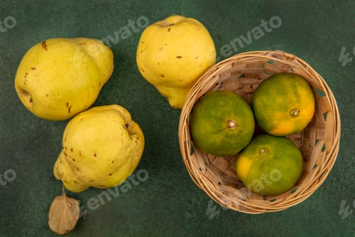 Preview: top view of delicious tangerines on a bucket with quinces on a green background