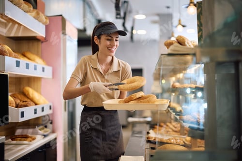 Preview: Happy woman arranging freshly baked pasty while working in a bakery.
