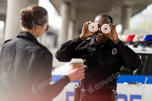 Preview: african american police officer pretending doughnuts as his eyes to amuse his partner