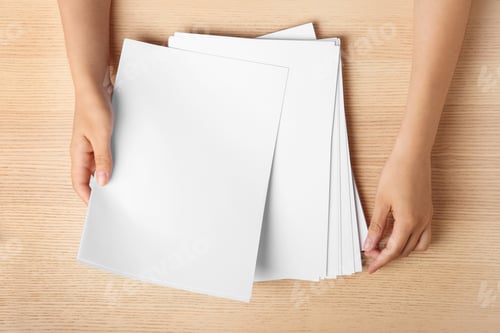 Preview: Woman holding blank paper sheets for brochure at wooden table, top view. Mock up
