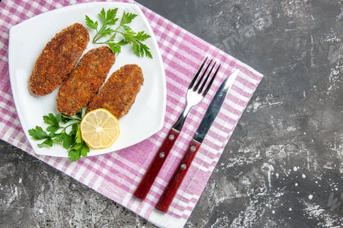 Preview: top view cutlets lemon slice parsley on white plate fork and knife kitchen towel on grey background