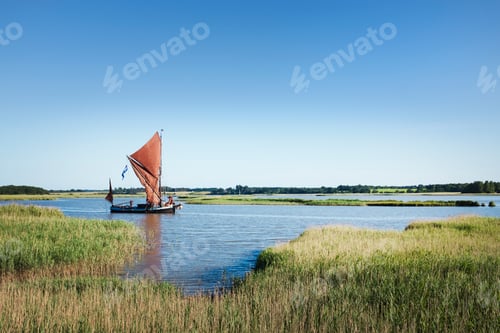 Preview: Traditional sailing boat with red sails and a gaff rig, a sailing smack on the water on a reed bed