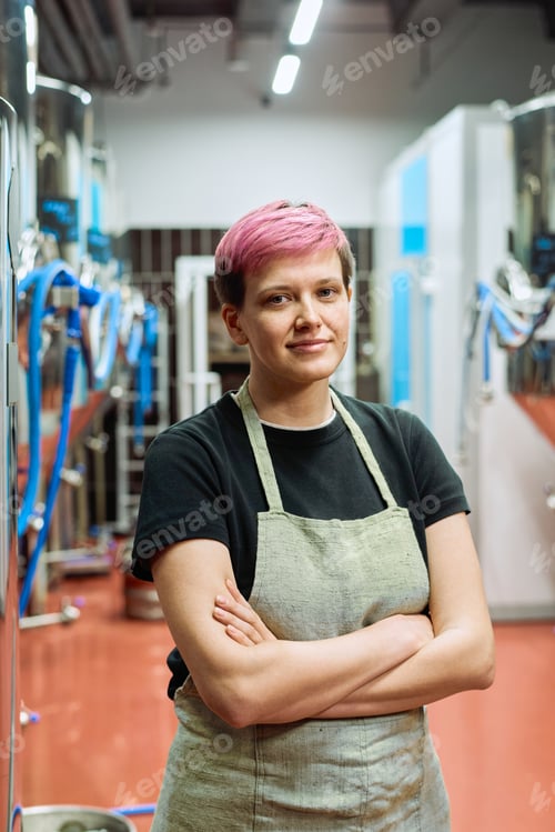 Preview: Young worker of beer production factory standing against large machines