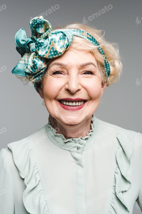 Preview: beautiful senior woman in stylish vintage shirt and headband isolated on grey
