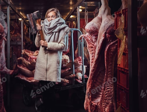 Preview: Blond female in a warm jacket in a meat freezer storage.