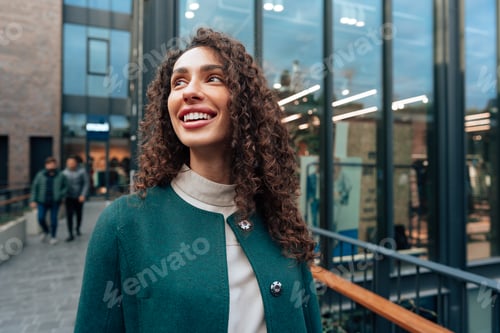 Preview: Portrait of young woman in green coat with curly hair in the city