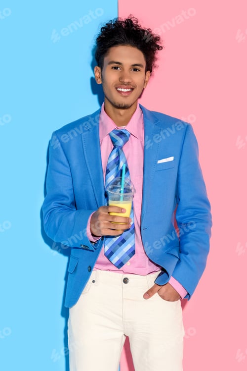 Preview: portrait of smiling african american man with glass of juice against pink and blue wall