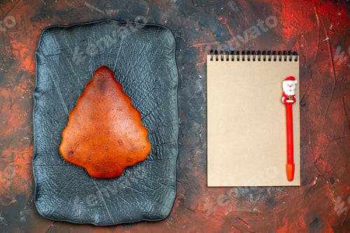Preview: top view cake on black platter pen on notebook on dark red table