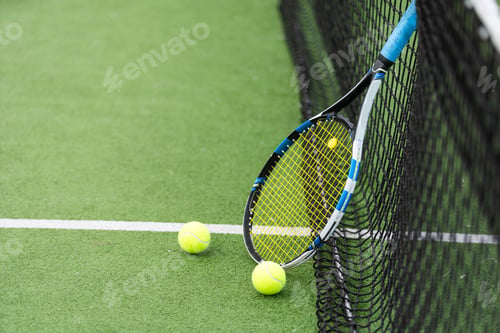 Preview: Tennis racket and tennis ball besides the net on outdoor tennis court.