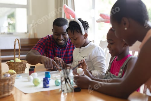 Preview: African american parents with son and daughter wearing bunny ears painting colourful eggs