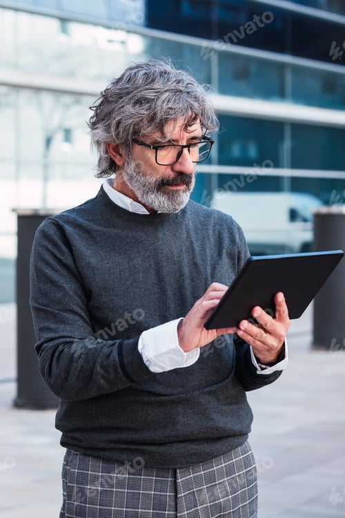 Preview: Mature handsome business man using a digital tablet outside office building