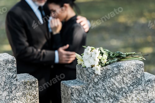 Preview: selective focus of bouquet on tombstone near man hugging woman