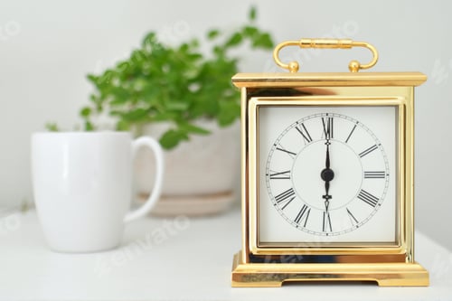 Preview: A gold clock timepiece with roman numerals setting on a dresser with white mug & plant