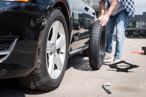 Preview: cropped view of man rolling new tire and fixing broken auto, car insurance concept