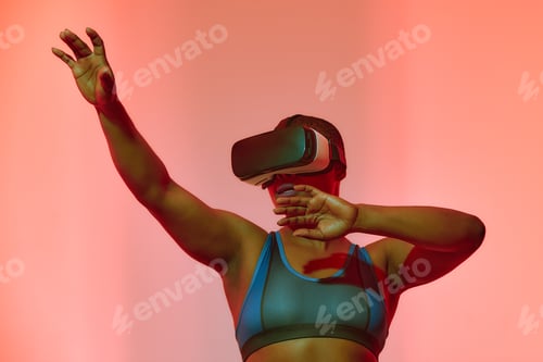 Preview: African american woman streamer playing video game using virtual reality glasses at gaming room