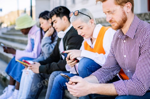 Preview: Multiracial young friends using smart phones sitting outdoors