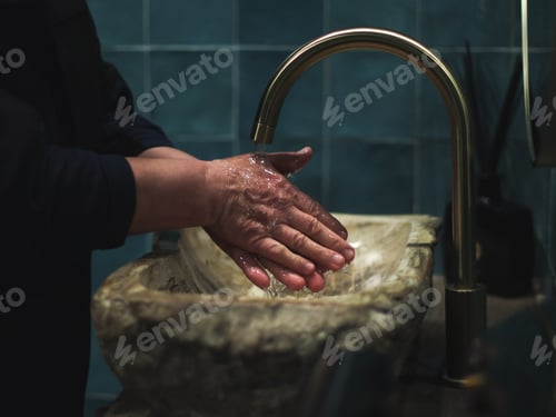 Preview: Elderly senior lady in black clothes washes her hands under the tap in the stone washbasin