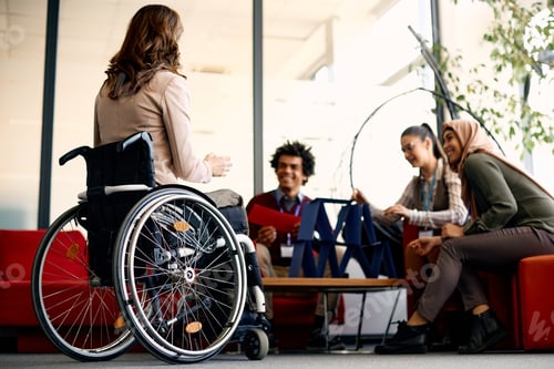 Preview: Rear view of businesswoman in wheelchair and her colleagues building house of cards in the office.