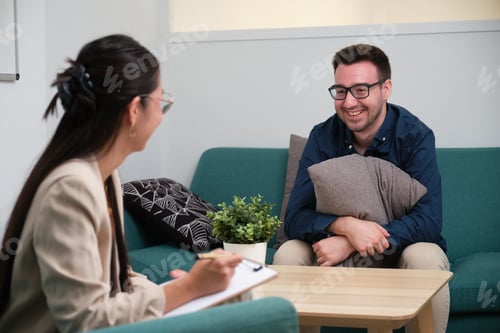 Preview: Asian female psychologist and caucasian man patient laughing at therapy.