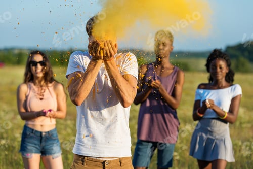Preview: young multiethnic friends blowing powder from palms at holi festival