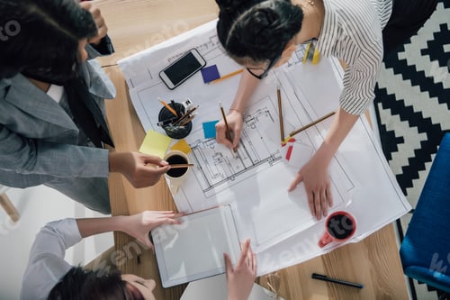 Preview: Overhead view of professional young architects working with blueprints and digital tablet