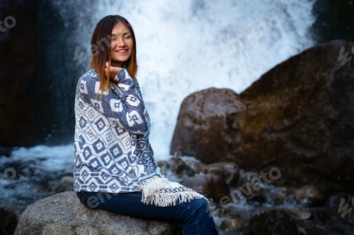 Preview: Beautiful young woman hiker sitting near waterfall