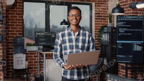 Preview: Portrait of african american programer standing working on laptop looking up and smiling