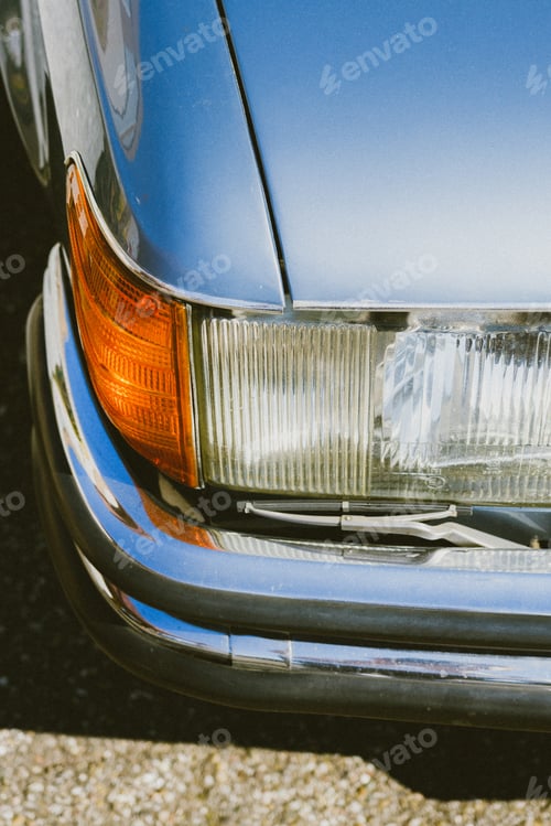 Preview: Vertical shot of the headlight of a vintage car parked outdoors on a sunny day