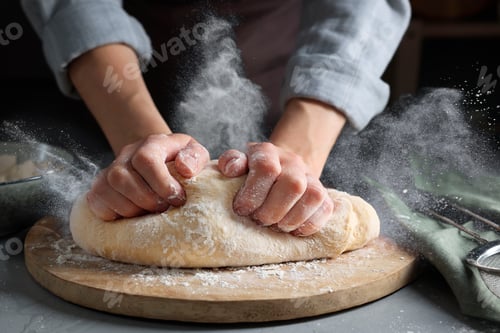 Preview: Woman kneading dough at grey table, closeup. Cloud of flour